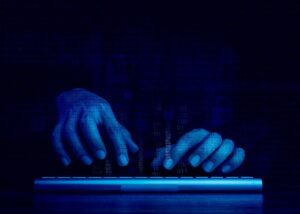 Hacker's hands working with keyboard computer on dark blue tone background.